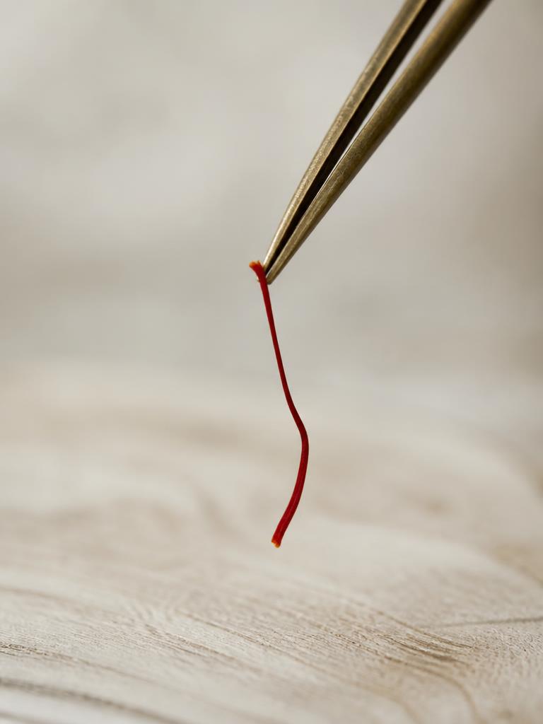 A single saffron thread held mid-air by aged brass tweezers on an oak table.